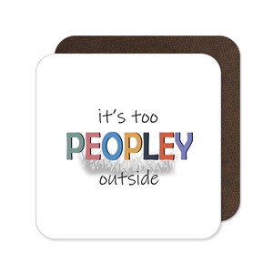 May include: A white square coaster with the text "it's too PEOPLEY outside" in colorful letters. The coaster has a brown, square backing.