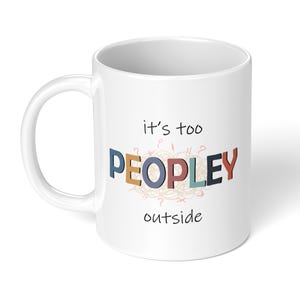 May include: White ceramic mug with the text "it's too PEOPLEY outside" in colorful, 3D-style lettering. The word "PEOPLEY" is in various colors, including blue, orange, and red. The mug has a standard handle.