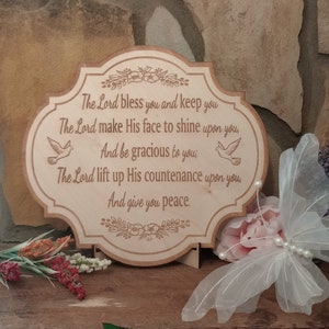 May include: A wooden sign with a carved design of flowers and doves. The sign has a quote from the Bible: "The Lord bless you and keep you. The Lord make His face to shine upon you, And be gracious to you; The Lord lift up His countenance upon you And give you peace."