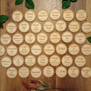 May include: A collection of wooden, circular ornaments with scalloped edges and various religious phrases engraved in a serif font. The ornaments are arranged on a wooden surface, with green leaves and a small floral arrangement.