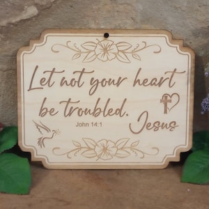 May include: Wooden sign with a light brown background and a white engraved design. The sign features a dove, a cross, a heart, and the text "Let not your heart be troubled. Jesus John 14:1".