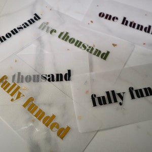 May include: Four transparent cards with gold glitter and black text. The cards read "five thousand", "five thousand", "one thousand fully funded", and "fully funded".