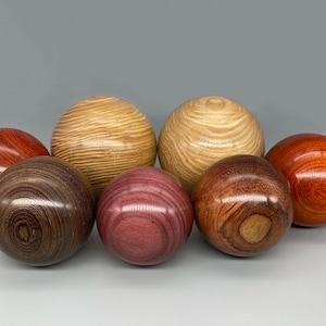 May include: Seven wooden spheres in shades of brown, red, and tan. The spheres have a smooth, polished finish, with visible wood grain patterns. Some spheres have a striped texture.