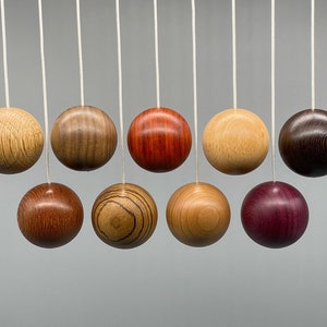 May include: Nine wooden balls of different colours and wood grains hang from white cords. The balls are suspended in a row against a grey background.