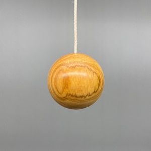May include: A spherical light pull made of light brown wood, showing a prominent wood grain pattern. It hangs from a white cord. This decorative item is designed for use in the home.