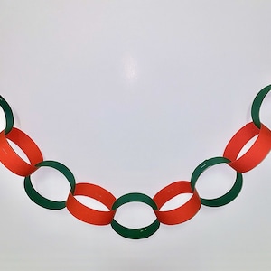 May include: A paper chain garland featuring alternating red and green links. The chain is arranged in a curved line against a white backdrop. The oval-shaped links are evenly spaced, creating a festive and decorative element.