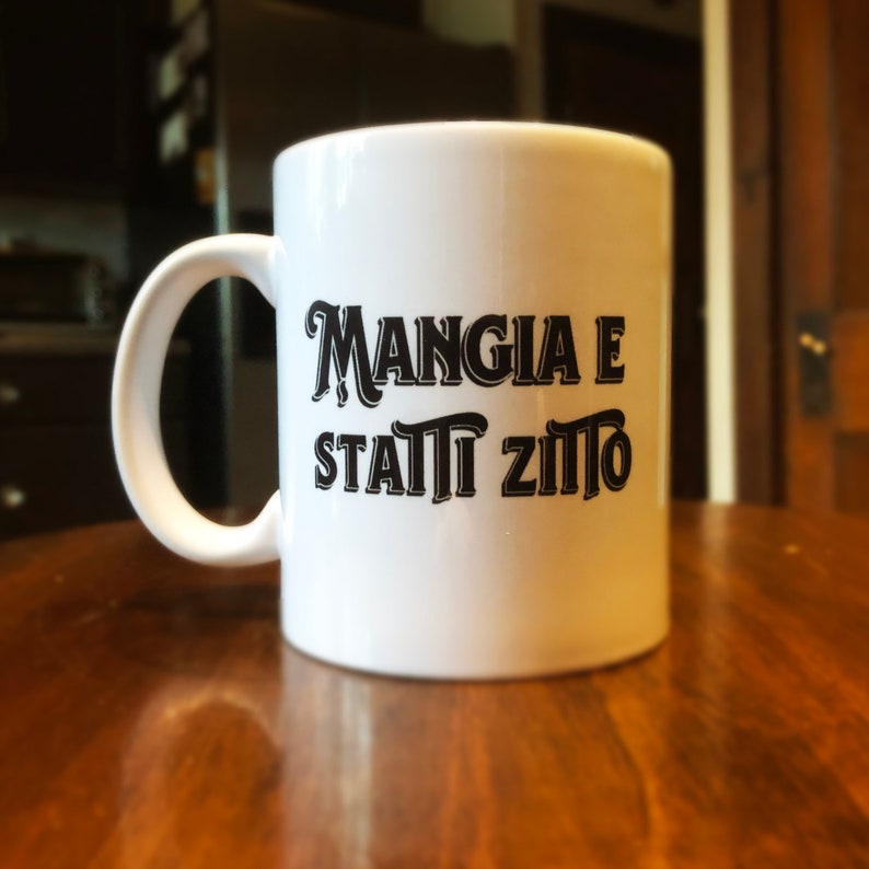 May include: White ceramic mug with a black inscription that reads "Mangia e stai zitto".