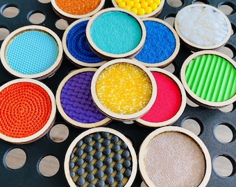 Peut inclure: Un ensemble de 12 cercles en bois avec différentes textures et couleurs. Les cercles sont disposés en demi-cercle sur une surface noire. Les textures comprennent une variété de tissus, de perles et d'autres matériaux.