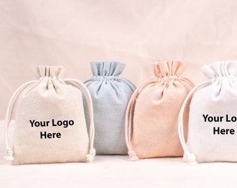May include: Four drawstring bags in different colors: natural, light blue, light pink, and white. Each bag has the text "Your Logo Here" printed on the front.