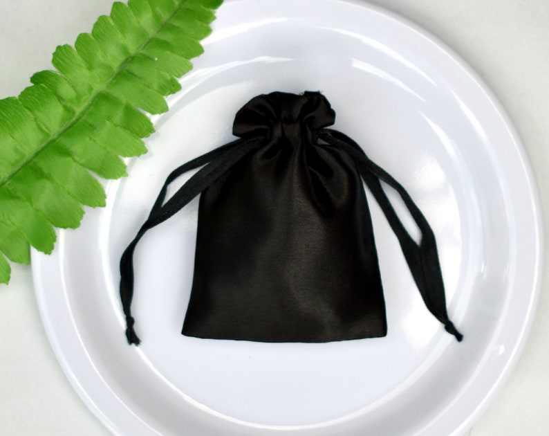 Peut inclure: Un sac en satin noir avec cordon de serrage sur un fond blanc. Le sac est fait d'un tissu doux et luxueux et a un design simple et &eacute;l&eacute;gant.