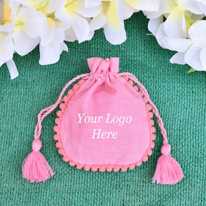 May include: Pink drawstring bag with white pom pom trim and tassels. The bag has the text "Your Logo Here" printed on the front.