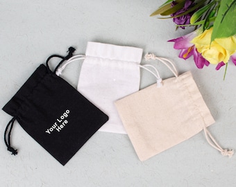 May include: Three drawstring bags, one black with the text "Your Logo Here", one white, and one beige.