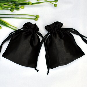 Peut inclure: Deux sacs en satin noir avec cordon de serrage sur un fond blanc. Les sacs sont faits d'un mat&eacute;riau doux et soyeux et ont un design simple et &eacute;l&eacute;gant.