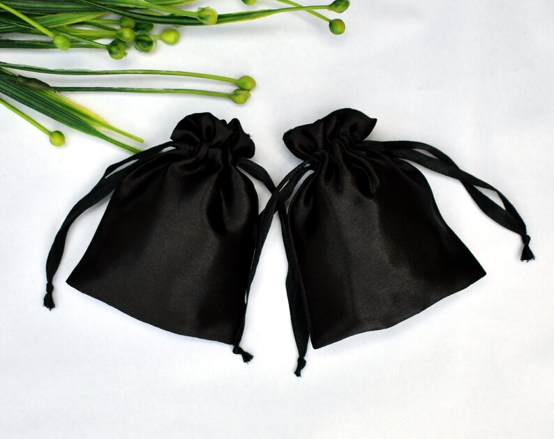 Peut inclure: Deux sacs en satin noir avec cordon de serrage sur un fond blanc. Les sacs sont faits d'un mat&eacute;riau doux et soyeux et ont un design simple et &eacute;l&eacute;gant.