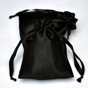 Peut inclure: Deux pochettes en satin noir avec cordon de serrage. Les pochettes sont faites d'un tissu doux et soyeux, avec une sensation lisse et luxueuse. Elles sont parfaites pour ranger de petits objets comme des bijoux, des cadeaux ou des faveurs.