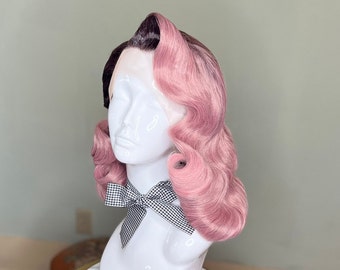 May include: A pink and black wig with a vintage style, featuring large, loose curls. The wig is styled with a side part and is worn on a mannequin head.
