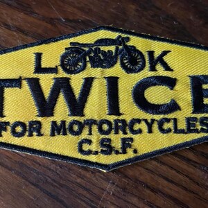 May include: Yellow and black embroidered patch with the text "LOOK TWICE FOR MOTORCYCLES C.S.F." and a motorcycle graphic. The patch has a black border and is in a hexagonal shape.