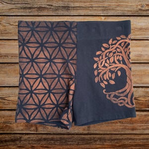 May include: Black shorts with a geometric pattern on one leg and a tree of life design on the other leg. The pattern is in a burnt orange colour.