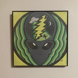 May include: A framed illustration of an alien with a green and yellow background. The alien's head is filled with a black and white image of a lightning bolt, a mountain, a crescent moon, and a UFO.
