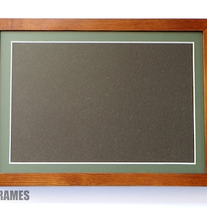 May include: A wooden picture frame with a green mount and a white inner border. The frame is a light brown colour and has a smooth finish.