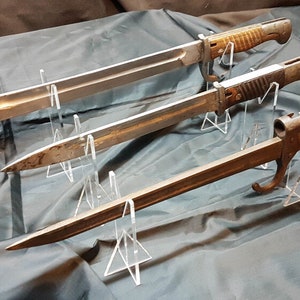 May include: Three antique bayonets displayed on clear acrylic stands. The bayonets are in various states of wear and have wooden handles. The bayonets are arranged in a staggered formation.