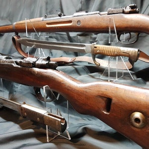 May include: Two wooden rifles with bayonets on display stands. The rifles are brown and have metal accents. The bayonets are silver and have wooden handles.