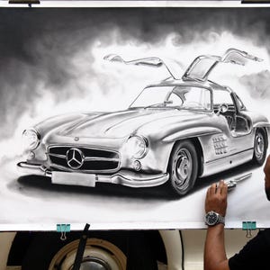 May include: A black and white drawing of a classic Mercedes-Benz 300 SL Gullwing sports car. The car is depicted with its doors open, and the artist is shown in the background, working on the drawing.