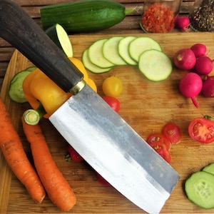 Peut inclure: Un gros plan d'une planche à découper en bois avec une variété de légumes, dont des carottes, des concombres, des radis, des tomates et des poivrons. Un grand couteau de chef argenté avec un manche en bois foncé est posé sur la planche.
