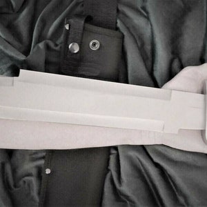 May include: A long, silver blade with a black handle and a black and white stripe on the handle. The blade is held in a person's hand.