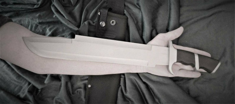 May include: A long, silver blade with a black handle and a black and white stripe on the handle. The blade is held in a person's hand.