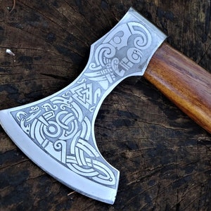 Può includere: Un'ascia d'argento con manico in legno. La testa dell'ascia è decorata con intricati motivi di nodi celtici.
