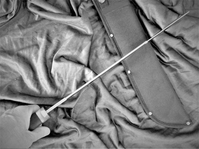 May include: A black and silver machete with a black nylon sheath. The machete is partially visible in the sheath, with the handle and blade extending out.