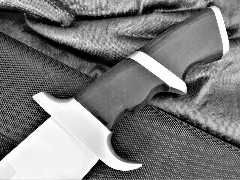 May include: A black and silver knife with a textured handle. The knife is lying on a black fabric background.