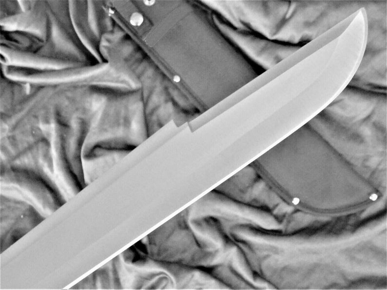 May include: A large, silver, single-edged blade with a black leather sheath. The blade is curved and has a sharp point. The sheath has a snap closure and is decorated with stitching.