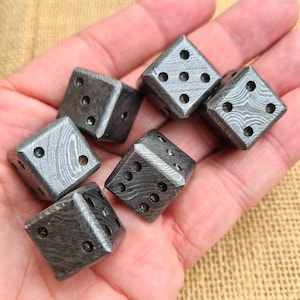 Könnte beinhalten: Sechs graue Würfel mit einem einzigartigen Muster werden in einer Hand gezeigt. Jeder Würfel hat eine unterschiedliche Anzahl schwarzer Punkte, von eins bis sechs. Die Würfel bestehen aus einem metallischen Material.