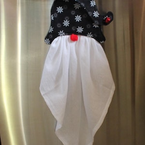 May include: A novelty snowman kitchen towel hanging on a stainless steel appliance handle. The towel has a black hat with white snowflakes, a red pom-pom nose, and a white body.