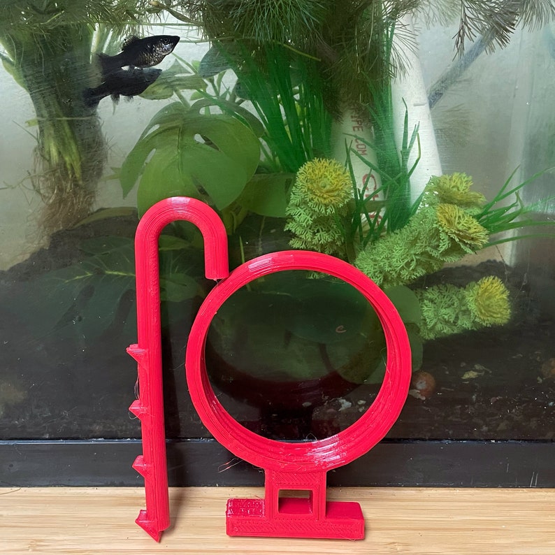 May include: A bright red plastic fish tank cleaning tool with a round brush and a long handle with spikes. The tool is designed to clean the sides and bottom of a fish tank.