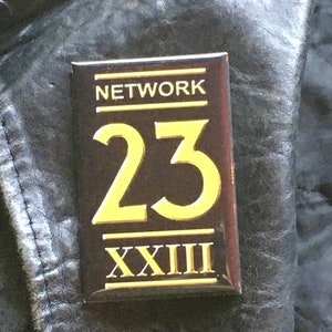 May include: A black and gold rectangular pin with the text "NETWORK" and the number "23" in gold. The number "XXIII" is also in gold below the number "23".