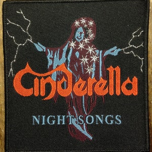 May include: A black fabric patch with a silver lightning bolt design and the band name "Cinderella" in orange lettering. The text "Night Songs" is below the band name in blue lettering. A blue and purple figure with a silver halo is in the center of the patch.
