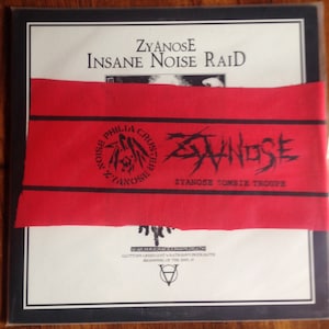 Peut inclure: Une pochette d'album carrée avec le texte "ZyanosE Insane Noise Raid" et une bande rouge sur le devant. La bande rouge porte le texte "Zyanose Zombie Troupe" et un logo circulaire. Le bas de la pochette porte le texte "War Nukerace Chaos Death".