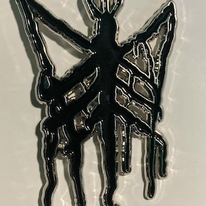 Peut inclure: Épingle en métal argenté avec un motif d'insecte noir stylisé. L'insecte a un corps et des ailes avec un effet dégoulinant. L'épingle est probablement un accessoire décoratif, peut-être pour une veste, un sac ou un chapeau.