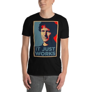 Puede incluir: Una camiseta negra con un gráfico rojo, blanco y azul de la cara de un hombre y el texto "IT JUST WORKS".