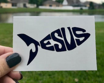 May include: A white sticker with a blue fish silhouette. The fish is made up of the word "JESUS" in a stylized font.