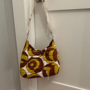 May include: A brown and yellow quilted shoulder bag with a white strap and a geometric pattern.