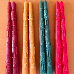 May include: Set of six taper candles with a nutcracker design. The candles are in red, green, and yellow.