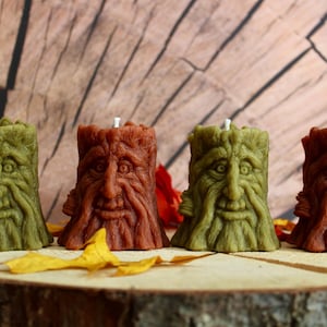 May include: Four handmade candles shaped like tree stumps with faces. Two candles are green and two are brown.