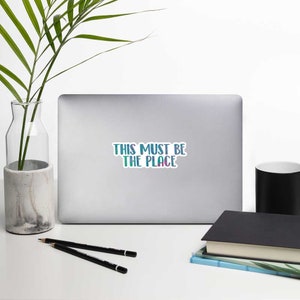May include: A laptop computer with a sticker that says "This must be the place" in a blue and green gradient.