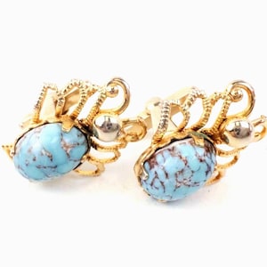May include: A pair of gold-toned cufflinks featuring oval, turquoise-colored stones with brown veining. The cufflinks have an ornate, openwork design with a small silver-colored sphere on each. The background is white.