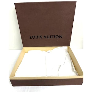 May include: Open brown cardboard box with the words "LOUIS VUITTON" printed on the inside lid. The box is lined with beige paper and contains white tissue paper. The box is open and ready for use.