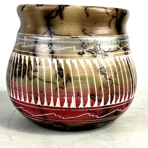 May include: A handcrafted, decorative ceramic pot with a wide, rounded body and a slightly flared rim. The pot features a color scheme of brown, red, and white, with a unique pattern of vertical white lines and wavy designs. The pot is approximately 5 inches in height.